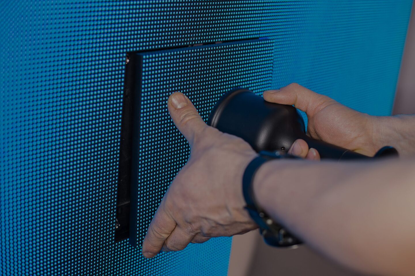Zwei Hände halten einen schwarzen, runden Gegenstand vor einem blauen, punktierten Hintergrund.