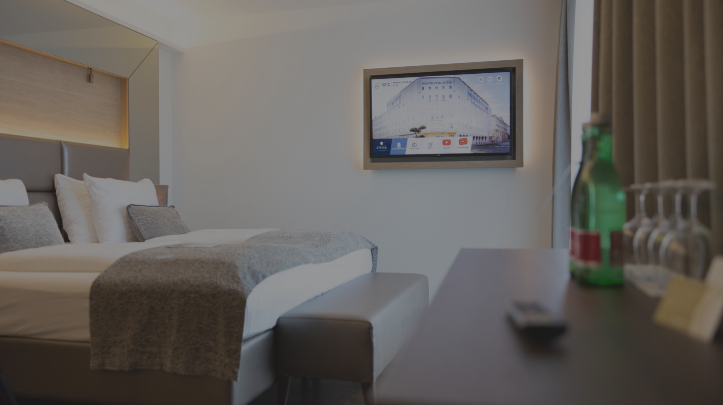 Ein modern eingerichtetes Hotelzimmer mit einem Bett, einem Fernseher an der Wand und einer Minibar auf dem Nachttisch.