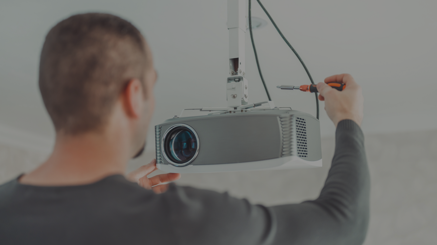 Mann hält einen Projektor und arbeitet mit einer Schraubendreher.